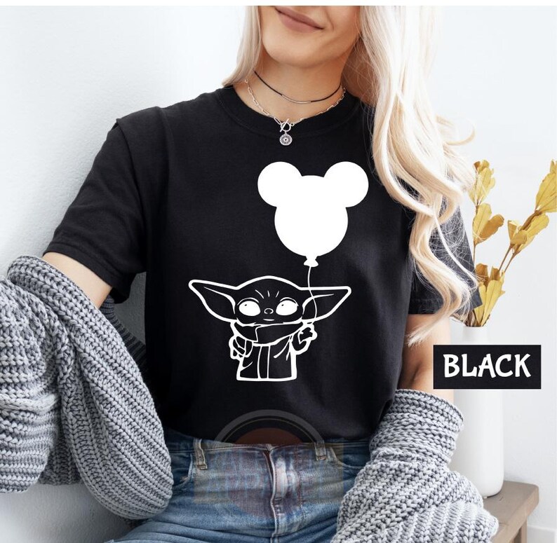 A woman wearing a black t-shirt with a white graphic of a character holding a balloon, along with a necklace.