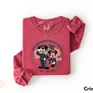 A red long-sleeved t-shirt with a graphic design featuring Minnie Mouse and Mickey Mouse in military uniforms, along with a patriotic theme.