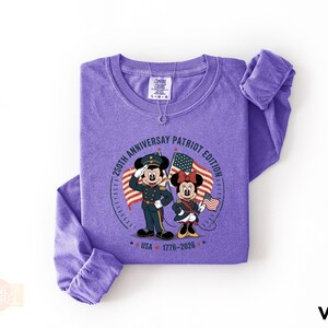 A purple long-sleeved t-shirt with a graphic design featuring Minnie Mouse and Mickey Mouse, along with text and a date.