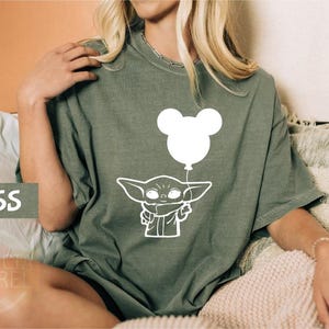 A woman wearing a green t-shirt with a white graphic of a baby character holding a balloon.