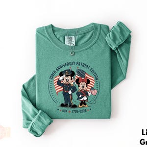 A green long-sleeved t-shirt with a graphic design featuring two cartoon characters, Minnie Mouse and Mickey Mouse, holding American flags and standing in front of a clock.