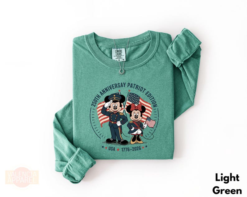 A green long-sleeved t-shirt with a graphic design featuring two cartoon characters, Minnie Mouse and Mickey Mouse, holding American flags and standing in front of a clock.