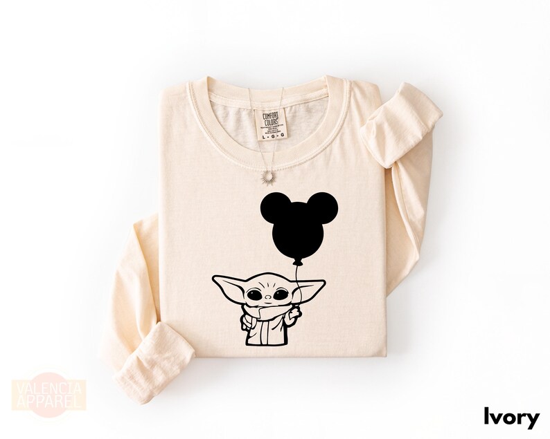 A beige t-shirt with a graphic design featuring a cartoon character holding a balloon with a Mickey Mouse face.