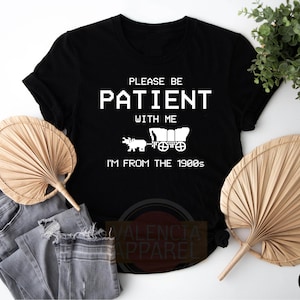 a black t - shirt that says please be patient with me i'm from