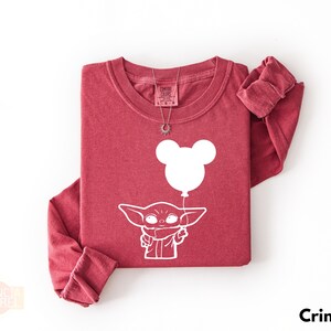 A red long-sleeved t-shirt with a white graphic design depicting a cartoon character holding a balloon.
