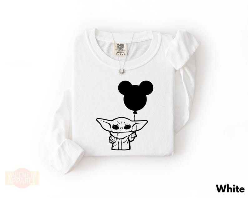 A white long-sleeved t-shirt with a black graphic design depicting a young alien character holding a balloon.