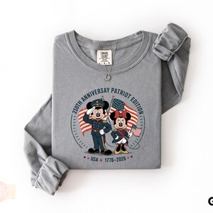 A gray long-sleeved t-shirt with a graphic design featuring two cartoon characters, Minnie Mouse and Mickey Mouse, holding American flags and standing in front of a clock.