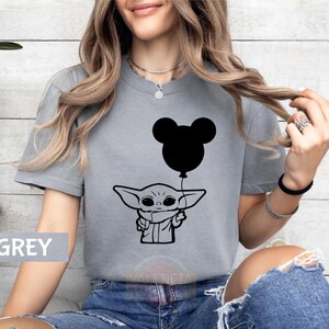 A woman wearing a grey t-shirt with a graphic of a young child holding a balloon, along with a Mickey Mouse balloon.