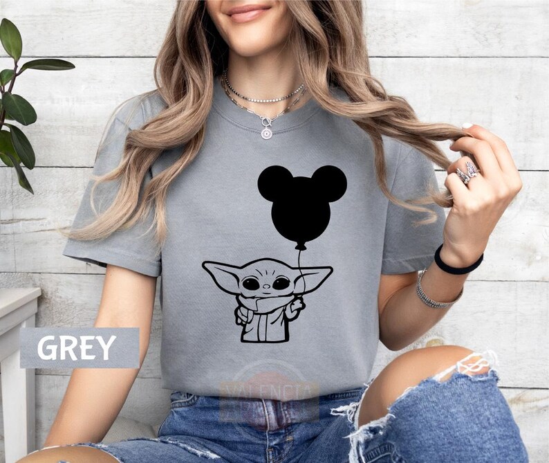 A woman wearing a grey t-shirt with a graphic of a young child holding a balloon, along with a Mickey Mouse balloon.