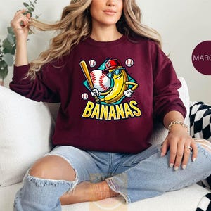 a woman sitting on a couch wearing a maroon sweatshirt