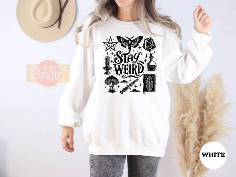 a woman wearing a white sweatshirt with the words stay weird on it