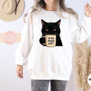 a woman wearing a white sweatshirt with a black cat holding a cup of coffee