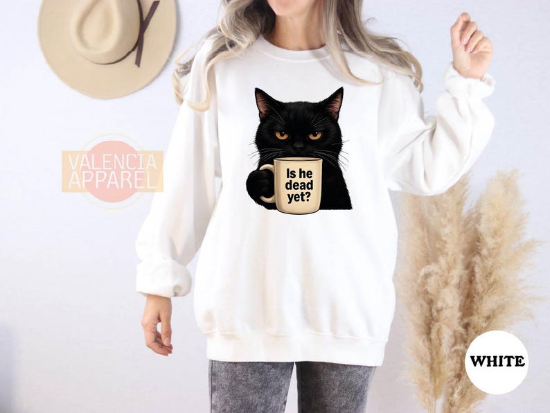 a woman wearing a white sweatshirt with a black cat holding a cup of coffee