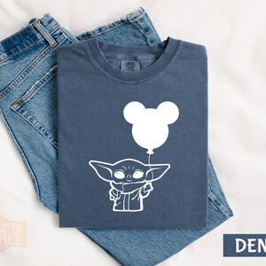 a blue t-shirt with a white graphic design depicting a young child holding a balloon, along with a pair of blue jeans.