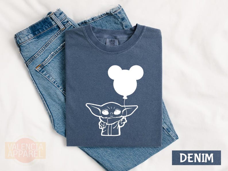 a blue t-shirt with a white graphic design depicting a young child holding a balloon, along with a pair of blue jeans.