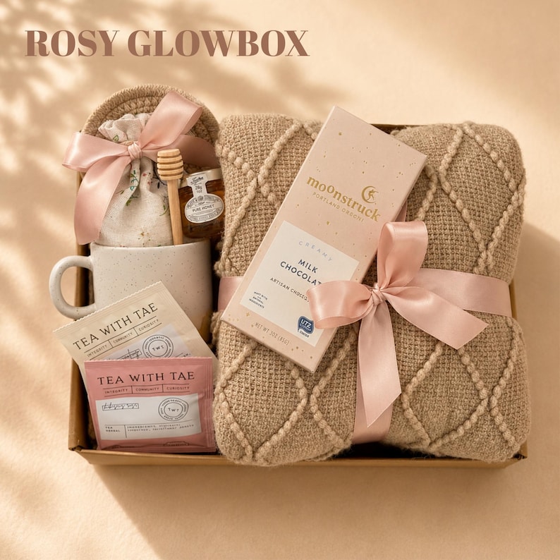 May include: A gift box labeled ROSY GLOWBOX containing a beige textured throw blanket tied with a pink ribbon, a Moonstruck milk chocolate bar, a speckled ceramic mug, a small jar of honey with a wooden dipper, and two Tea With Tae tea packets.