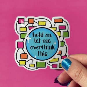 May include: A white sticker with a blue circle in the center. The circle has the text "hold on, let me overthink this" in black. The sticker also has a colorful diagram of connected boxes.
