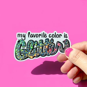 May include: A white sticker with the text "my favorite color is glitter" in black lettering. The word "glitter" is written in a large, stylized font and is covered in iridescent glitter.