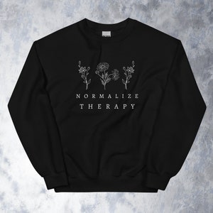 Puede incluir: Sudadera negra con texto blanco que dice "Normalizar la terapia" y un diseño floral.