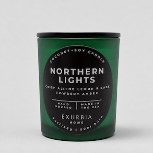 Puede incluir: Una vela de coco y soja en un frasco de vidrio verde oscuro con tapa negra y etiqueta circular negra. La etiqueta dice COCONUT + SOY CANDLE, NORTHERN LIGHTS, CRISP ALPINE LEMON & SAGE, POWDERY AMBER, 198 g | 50 hr burn, EXURBIA HOME, HAND POURED.