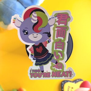 May include: A sticker featuring a purple unicorn character winking and giving a peace sign. The sticker has Japanese text and the phrase "I THINK YOU'RE NEAT!" in a green and pink font. The unicorn has a rainbow mane and is wearing a black skirt.