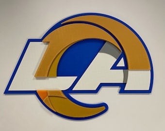Könnte beinhalten: Ein blaues, weißes und goldenes Los Angeles Rams Logo mit den Buchstaben "LA" in Weiß und einem goldenen Widderhorn.