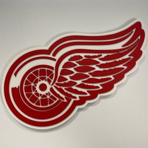 May include: Red and white Detroit Red Wings logo with a wing and a wheel. The logo is made of a thick, flat material.