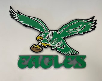May include: Green and white 3D eagle with a football in its talons, flying above the word "EAGLES" in green and gray letters.