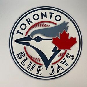 May include: A white, blue, and red circular logo with the text "Toronto Blue Jays" around the edge. A blue jay with a red maple leaf is in the center.