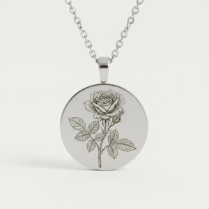 Peut inclure: Collier argenté avec un pendentif rond gravé d'une rose. Le pendentif présente une illustration détaillée d'une rose avec des feuilles et une tige. La chaîne est de style maillon délicat, adaptée au quotidien. Le pendentif mesure environ 3 cm de diamètre.