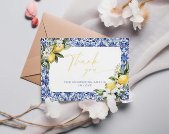 May include: A thank you card with a blue and white tile border, featuring lemons and white flowers. The card says "Thank you" in gold script, with the text "FOR SHOWERING AMELIA IN LOVE" below.