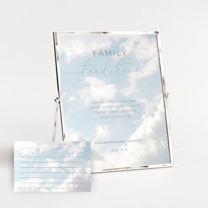 May include: A white framed sign with a blue sky and white clouds background. The sign says "FAMILY traditions" and "Please take a card and write down your favorite family tradition from your childhood". Below the sign is a white card with a blue sky and white clouds background. The card says "My favorite tradition".