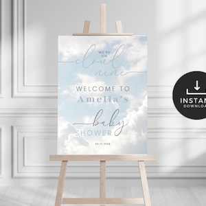 May include: A baby shower welcome sign with a blue sky and white clouds background. The text reads "We're on cloud nine. Welcome to Amelia's baby shower. 03.17.2024."
