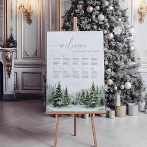 May include: A wedding seating plan displayed on a wooden easel. The sign says "welcome" and "please find your seat". The bottom of the sign features a watercolour painting of evergreen trees and a snowy landscape. The sign is in a room with a Christmas tree.