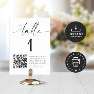 May include: A white table number card with black calligraphy that reads "table 1". A black and white QR code is printed below the table number with the text "Please share your photos with us simply scan the QR code and upload. Thank you!"