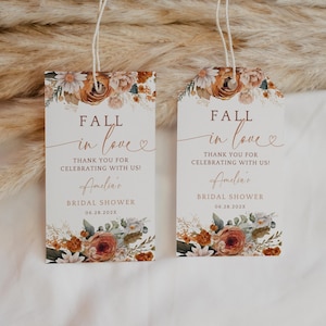 Può includere: Due etichette per bomboniere di addio al nubilato a tema autunnale con motivi floreali in tonalità arancio, marrone e bianco. Il testo recita "Fall in love" e "Grazie per aver festeggiato con noi!" con il nome della sposa e la data della doccia.