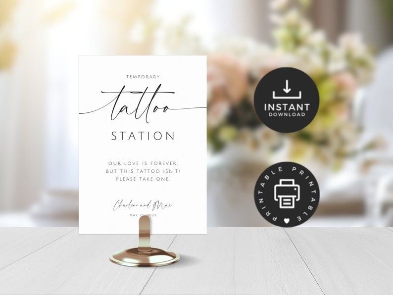 May include: A white sign for a temporary tattoo station, featuring elegant script lettering. The sign says "Temporary Tattoo Station" and includes the text "Our love is forever, but this tattoo isn't, please take one." The sign is held by a gold metal stand.