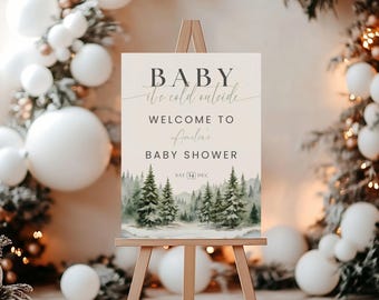 May include: A rectangular welcome sign for a baby shower displayed on a wooden easel. The sign features a watercolor forest scene at the bottom and text that reads: BABY it's cold outside, WELCOME TO Amelia's BABY SHOWER, and SAT 14 DEC.
