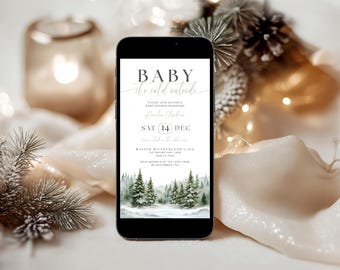 May include: A smartphone displaying a digital baby shower invitation with the text Baby It's Cold Outside. The design features a watercolor winter forest scene with pine trees and snow at the bottom, plus event details including date and location.