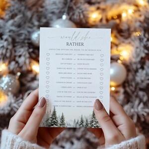 Puede incluir: Una tarjeta blanca con el texto "would she rather" en una fuente de escritura, sostenida por manos. La tarjeta enumera varias opciones, como "Mexican take out" y "Chinese take out". Una escena de bosque invernal está en la parte inferior.