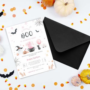 May include: A white baby shower invitation card with the text A LITTLE BOO IS ALMOST DUE, featuring illustrations of a ghost, a black cat, a cauldron, and pumpkins, paired with a black envelope and surrounded by scattered candy corn and pumpkins.