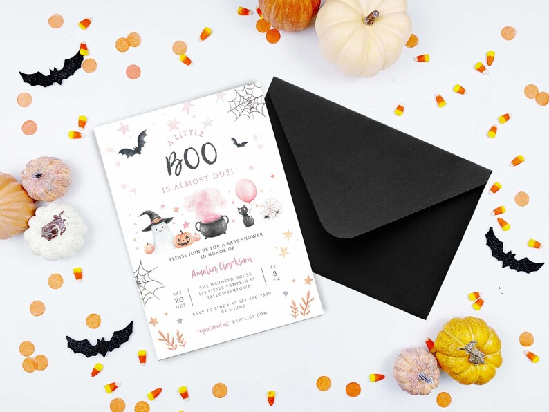May include: A white baby shower invitation card with the text A LITTLE BOO IS ALMOST DUE, featuring illustrations of a ghost, a black cat, a cauldron, and pumpkins, paired with a black envelope and surrounded by scattered candy corn and pumpkins.