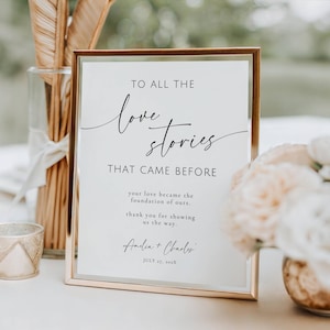 May include: A rectangular sign in a thin metallic gold frame featuring black printed text that reads: TO ALL THE love stories THAT CAME BEFORE, your love became the foundation of ours. thank you for showing us the way. Amelia + Charles JULY 27, 202X.