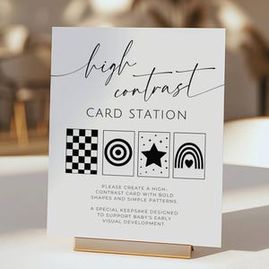 May include: A white rectangular sign with black text reading high contrast CARD STATION. Below are four black and white illustrations of a checkerboard, target, star, and rainbow. Additional text provides instructions for creating cards.