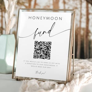 May include: A white sign with black text that reads "HONEYMOON fund" with a black and white QR code below. The text continues "If you would like to send us off with a donation to our honeymoon, it would make our day! Thank you!"