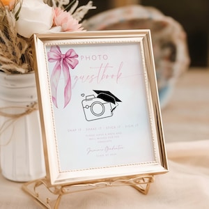 Könnte beinhalten: Ein goldener Rahmen mit weißem Hintergrund und einer rosa Aquarell-Schleife. Der Text "PHOTO GUESTBOOK" ist in rosa Schrift geschrieben. Der Text "SNAP IT, SHARE IT, STICK IT, SIGN IT" ist in Schwarz geschrieben. Der Text "PLEASE LEAVE A PHOTO AND WELL WISHES FOR OUR GRADUATE" ist in Schwarz geschrieben. Der Text "[Name] Graduation Class of 2023" ist in Schwarz geschrieben. Eine Schwarzweißillustration einer Kamera mit einer Abschluss-Kappe obenauf befindet sich in der Mitte des Rahmens.