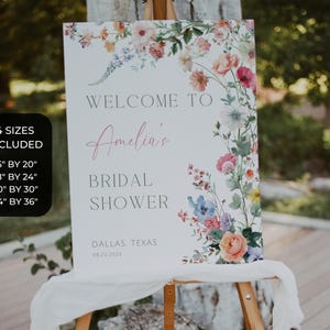 May include: A white sign with floral accents, announcing a bridal shower. The sign reads "Welcome to Amelia's Bridal Shower" with the location and date. Four size options are listed: 16" by 20", 18" by 24", 20" by 30", and 24" by 36".