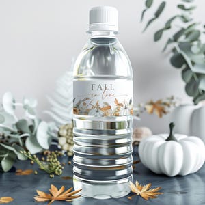 May include: A clear plastic water bottle with a white cap and a label that reads "FALL in love." The label features floral and pumpkin illustrations. The bottle is surrounded by fall-themed decorations, including pumpkins and leaves.