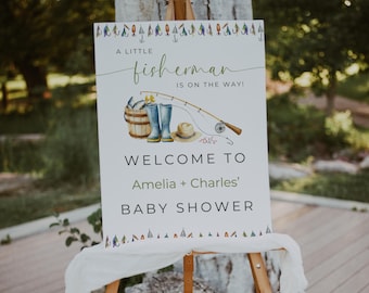 Op de afbeelding: Een wit bord met een groene en bruine illustratie van een hengel, laarzen en een emmer met vis. Het bord staat er: "Een kleine visser is onderweg!" en "Welkom op de babyshower van Amelia + Charles".