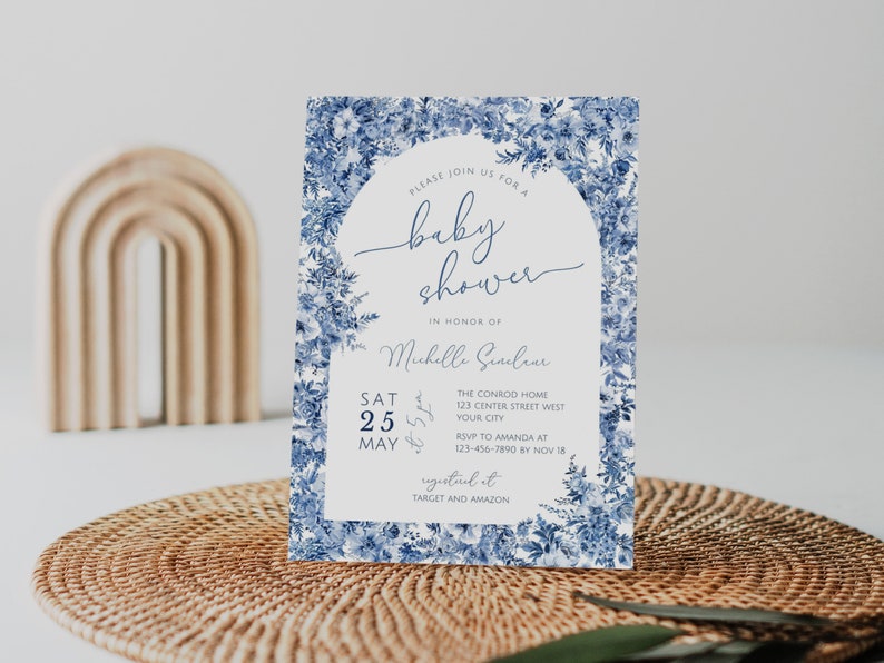 May include: A blue and white floral baby shower invitation with a white archway and the text "Please join us for a baby shower in honor of Michelle Sinclair. Sat 25 May. The Conrod Home 123 Center Street West Your City. RSVP to Amanda at 123-456-7890 by Nov 18. Registered at Target and Amazon."